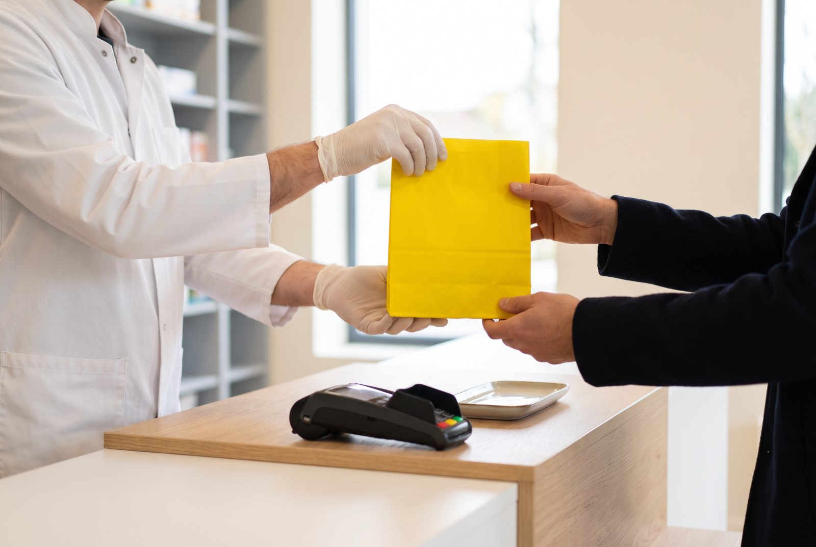 Pharmacien remettant un sac jaune à un patient au comptoir de l’officine